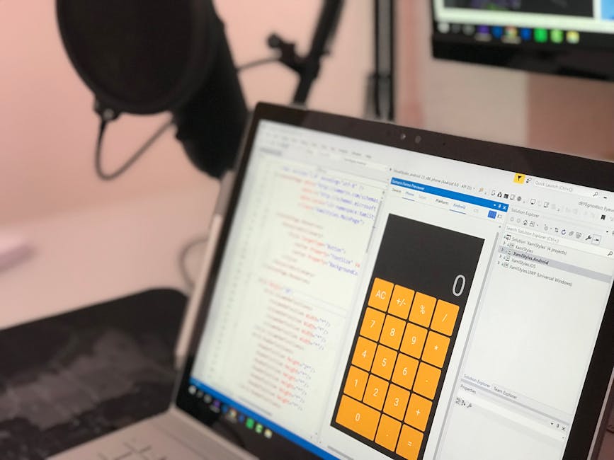A close-up photograph of a laptop computer situated on a desk, with its screen displaying lines of code in various colours on the left side and a large orange and black calculator interface on the rig